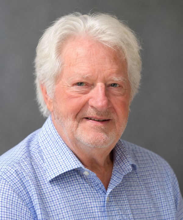 Portrait of Herman Schaap, smiling, with white hair and a short white beard, in a blue checked shirt against a grey background.